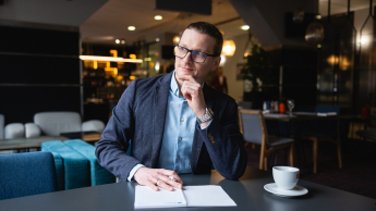Inżynieria oprogramowania w JavaScript (TypeScript) | Studia podyplomowe w Gdańsku | Uniwersytet WSB Merito w Gdańsku: Mężczyzna w ubraniu biznesowym siedzi przy biurku z filiżanką kawy
