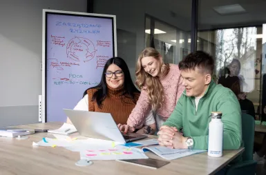 Zapraszamy na sesję, ale spokojnie – tylko zdjęciową! | Aktualności | Uniwersytet WSB Merito w Gdańsku: Studenci w bibliotece siedzą przy biurku i opracowują jakieś zagadnienie przy laptopie