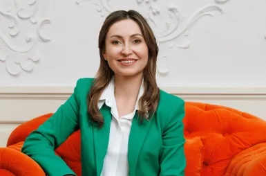 Wspólnie o przyszłości gospodarki | Aktualności | Uniwersytet WSB Merito w Gdańsku: Zdjęcie uśmiechniętej kobiety w zielonej marynarce na pomarańczowym fotelu
