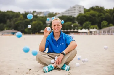 Zapraszamy na sesję, ale spokojnie – tylko zdjęciową! | Aktualności | Uniwersytet WSB Merito w Gdańsku: Student siedzi po turecku na plaży, wokół niego latają piłeczki