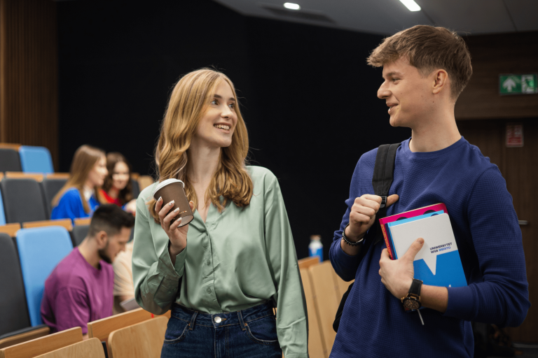 Przeniesienie z innej uczelni - szkolenie - do zmodyfikowania | Uniwersytet WSB Merito w Gdańsku: Studenci znajdują się na auli, Ci na drugim planie siedzą, a na Ci na pierwszym chłopak i dziewczyna stoją i rozmawiają