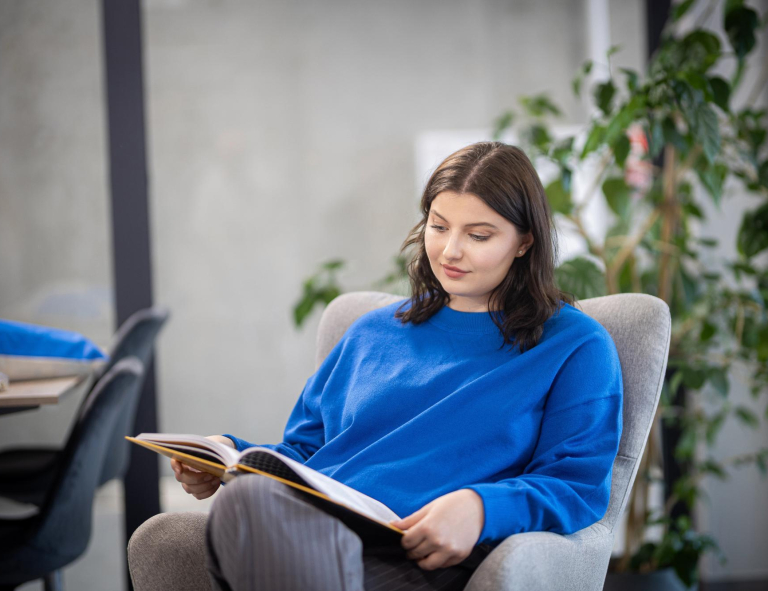 Biblioteka | Uniwersytet WSB Merito w Gdańsku: Studentka w przestrzeni biblioteki, siedzi w fotelu z książką