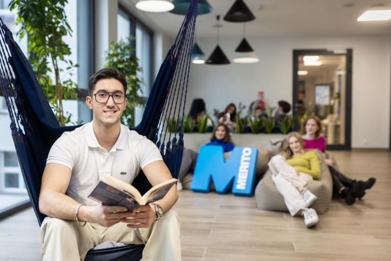 Negocjacje i mediacje w biznesie | Studia I stopnia w Gdańsku | Uniwersytet WSB Merito w Gdańsku: Student siedzi w hamaku i w rękach trzyma książkę, a za nim siedzą studentki