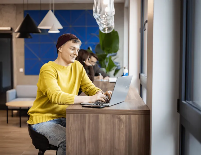 Information Technology | Studia I stopnia w Gdańsku | Uniwersytet WSB Merito w Gdańsku: Student siedzi przy laptopie, ma na sobie żółty sweter i fioletową czapkę