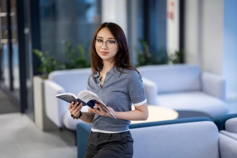 Stosunki międzynarodowe | Studia I stopnia w Gdańsku | Uniwersytet WSB Merito w Gdańsku: Studentka o azjatyckiej urodzie opiera się o kanapę i trzyma książkę