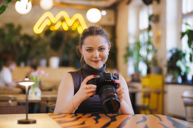 Komunikacja cyfrowa i media kreatywne | Studia II stopnia ze studiami podyplomowymi w Gdańsku | Uniwersytet WSB Merito w Gdańsku: Studentka w kawiarni trzymająca w ręku aparat fotograficzny