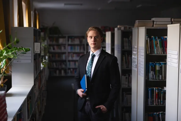 Projekty i usługi | Uniwersytet WSB Merito w Gdańsku: Student w garniturze we wnętrzu biblioteki