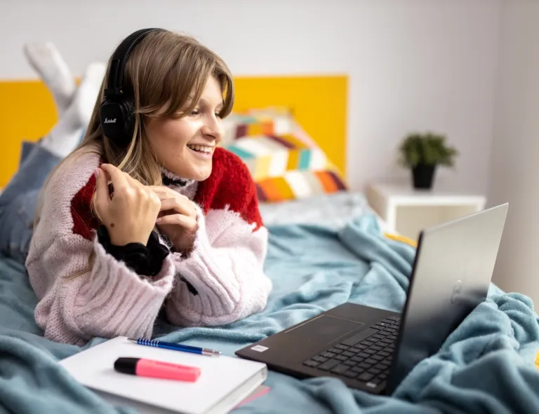 Informatyka | Studia I stopnia w Gdańsku | Uniwersytet WSB Merito w Gdańsku: Studentka leży na łóżku i uczestniczy w spotkaniu online