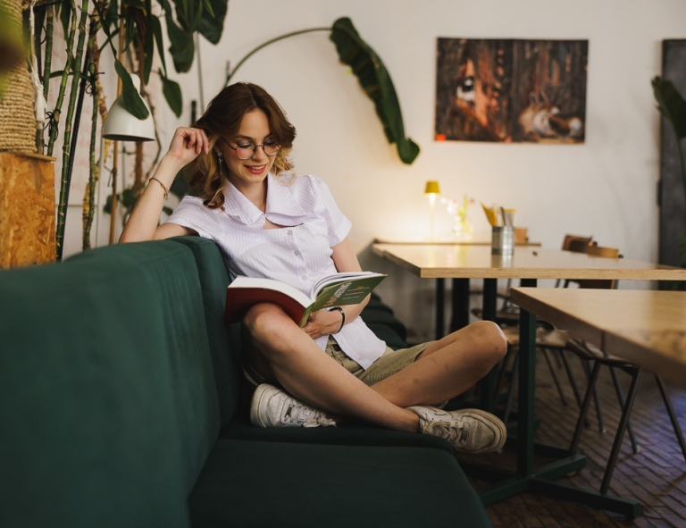 Specjalista kadr i płac z elementami technik coachingu | Studia II stopnia ze studiami podyplomowymi  | Uniwersytet WSB Merito w Gdańsku: Studentka na kanapie w kawiarni z książką