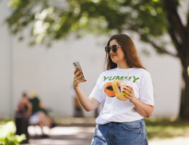 Zarządzanie turystyką doświadczeń | Studia II stopnia ze studiami podyplomowymi  | Uniwersytet WSB Merito w Gdańsku: Studentka latem z komórką i napojem w ręku