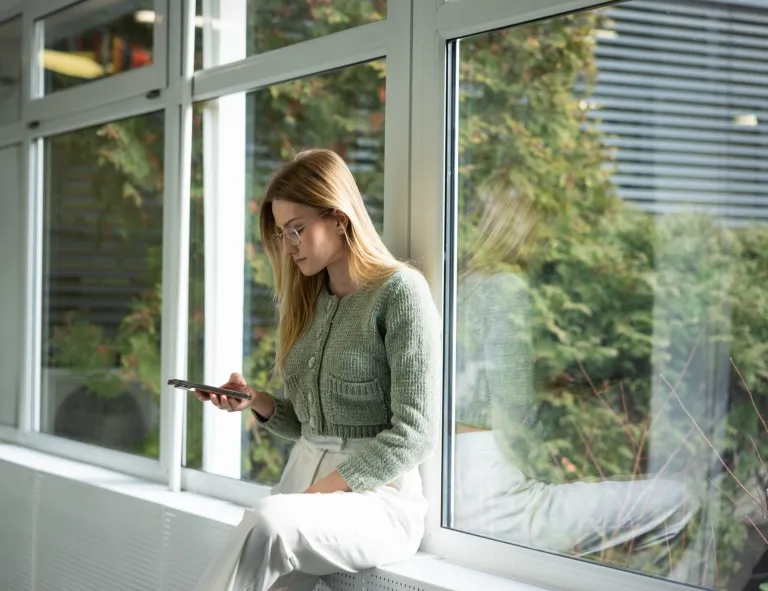 Psychokryminalistyka | Studia II stopnia w Gdańsku | Uniwersytet WSB Merito w Gdańsku: Dziewczyna opiera się o parapet i przegląda telefon