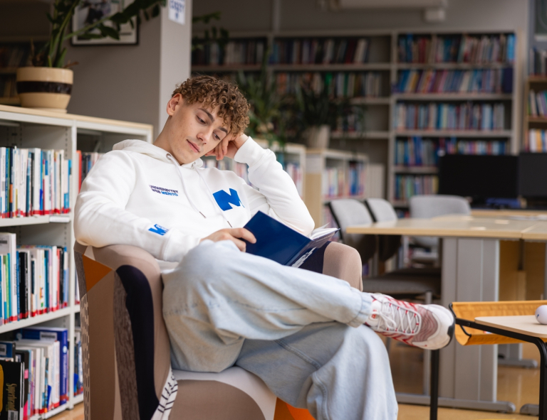 Programowanie desktop apps | Studia II stopnia ze studiami podyplomowymi  | Uniwersytet WSB Merito w Gdańsku: Student na fotelu czyta książkę w bibliotece