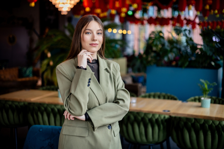 Dni otwarte wydziałów | Uniwersytet WSB Merito w Gdańsku: Zdjęcie biznesowe studentki w przestrzeni kawiarni. Młoda dziewczyna w oliwkowej marynarce