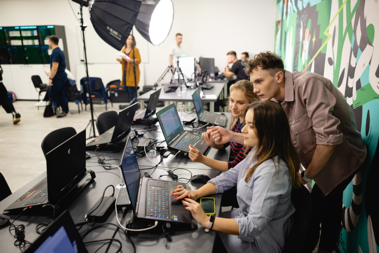 Inżynieria oprogramowania dla technologii kosmicznych | Studia I stopnia w Gdańsku | Uniwersytet WSB Merito w Gdańsku: Studenci w studio z komputerami, lampami i grafiką na ścianie