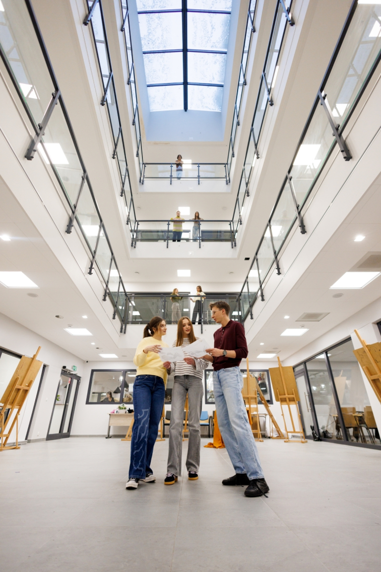 Marketing i komunikacja społeczna | Studia I stopnia w Gdańsku | Uniwersytet WSB Merito w Gdańsku: Studenci stoją pośrodku atrium. Zdjęcie z perspektywy żabiej z widokiem na architekturę budynku