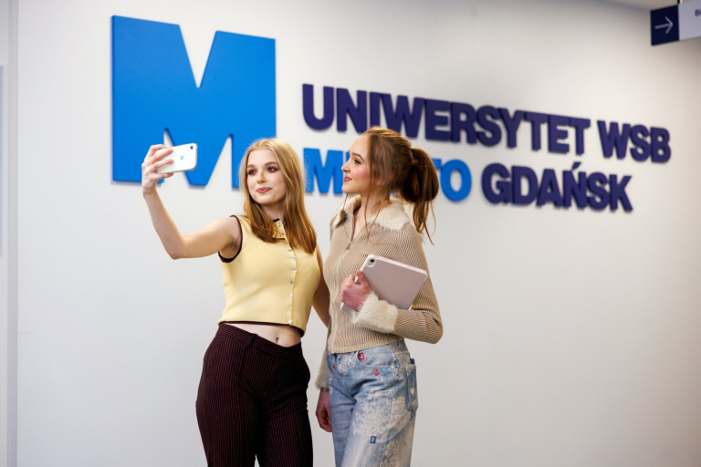 Czesne, stypendia i zniżki | Uniwersytet WSB Merito w Gdańsku: Studentki robią sobie selfie przy napisie UWSB Merito Gdańsk