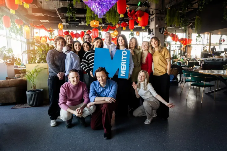 Zapraszamy na sesję, ale spokojnie – tylko zdjęciową! | Aktualności | Uniwersytet WSB Merito w Gdańsku: Zdjęcie grupowe studentów w industrialnej przestrzeni. Po środku trzymają sygnet logo Uczelni Merito