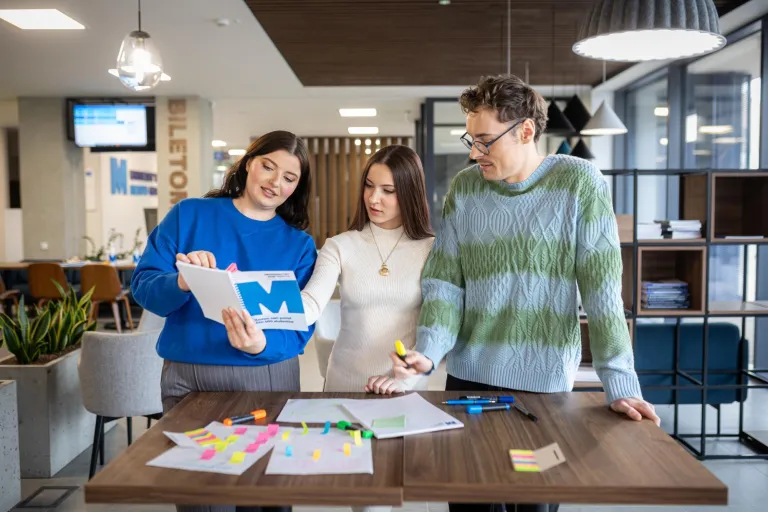 Tłumaczenia- język angielski | Studia II stopnia ze studiami podyplomowymi  | Uniwersytet WSB Merito w Gdańsku: Dwie studentki i student stoją nad stołem i wykonują zadanie