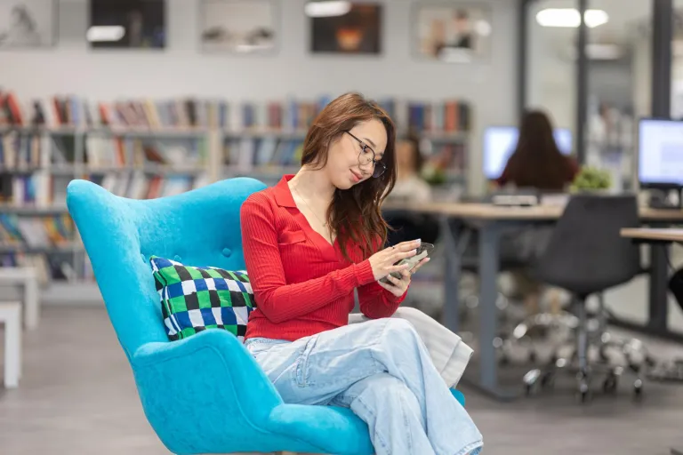 Sztuczna inteligencja w informatyce | Studia I stopnia w Gdańsku | Uniwersytet WSB Merito w Gdańsku: Studentka w bibliotece siedzi na wygodnym fotelu i korzysta z komórki