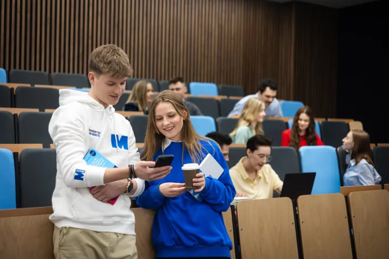 Psychologia menedżerska | Uniwersytet WSB Merito w Gdańsku: Studenci w auli, chłopak i dziewczyna pokazują sobie coś na komórce