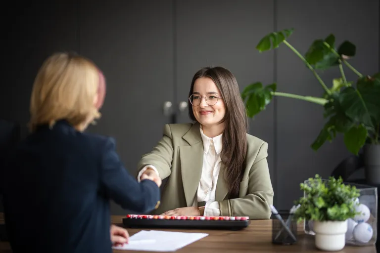 Menedżer administracji | Studia II stopnia ze studiami podyplomowymi  | Uniwersytet WSB Merito w Gdańsku: Dwie kobiety siedzą przy biurku i podają sobie ręce do uścisku dłoni