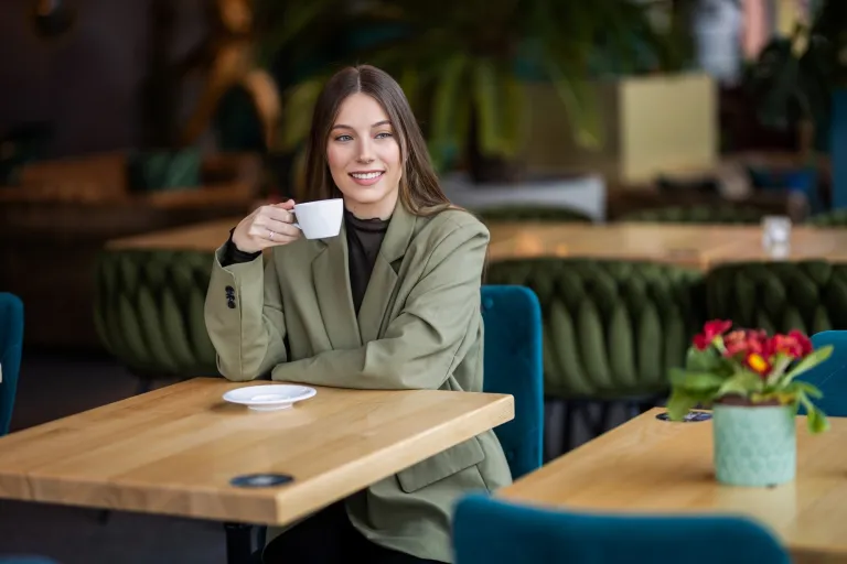 Psychologia w zarządzaniu – z certyfikatem FU | Studia II stopnia ze studiami podyplomowymi  | Uniwersytet WSB Merito w Gdańsku: Studentka w kawiarni z kawą, obok stoi kwiatek na stoliku