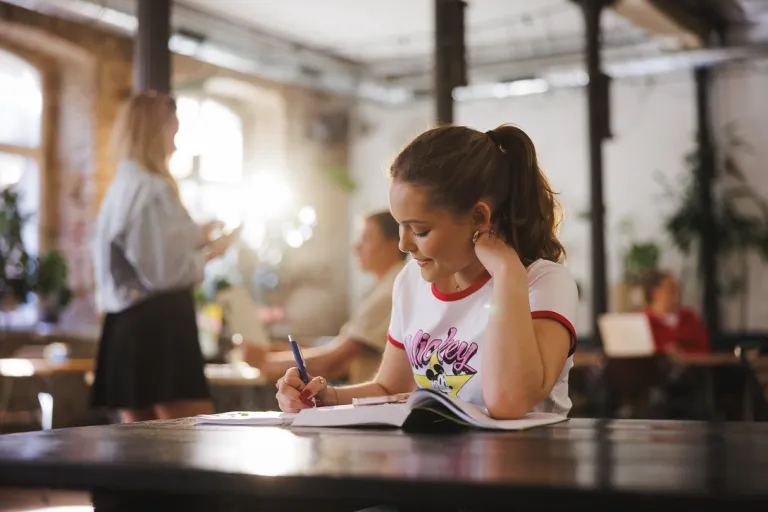 Terapia pedagogiczna z elementami integracji sensorycznej | Studia II stopnia ze studiami podyplomowymi  | Uniwersytet WSB Merito w Gdańsku: Zdjęcie studentki w kawiarni robiącej notatki 