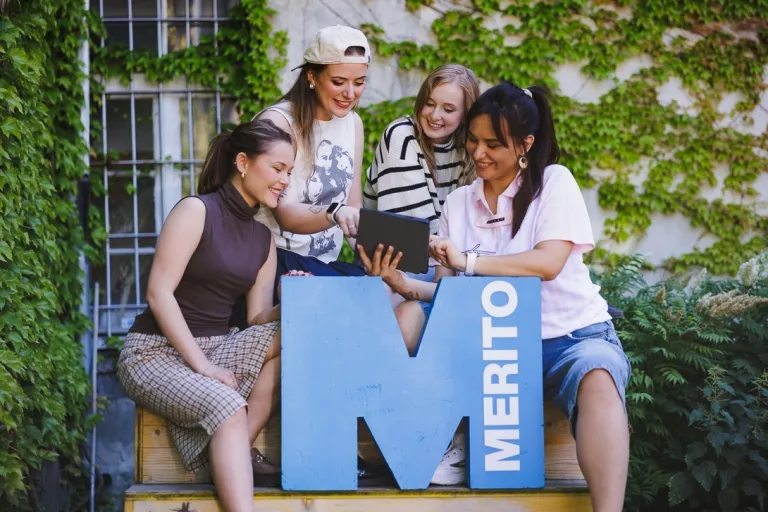 ESG i zrównoważona odpowiedzialność biznesu | Studia II stopnia ze studiami podyplomowymi  | Uniwersytet WSB Merito w Gdańsku: Studentki przy sygnecie M, patrzą w telefon, siedzą na schodach przy kawiarni