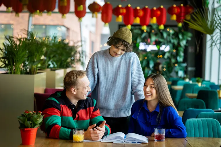 Prompting i optymalizacja systemów AI | Studia I stopnia w Gdańsku | Uniwersytet WSB Merito w Gdańsku: Studenci w kawiarni przy książce