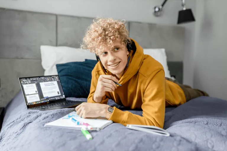 Psychologia wychowawcza | Studia jednolite magisterskie w Gdańsku | Uniwersytet WSB Merito w Gdańsku: Student leży na łóżku z notatkami i laptopem