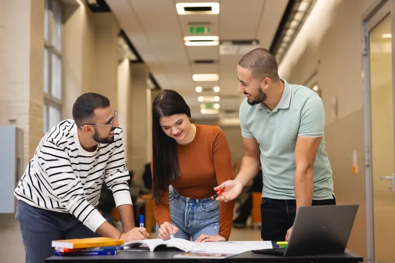 Lean w cyfrowych łańcuchach dostaw | Uniwersytet WSB Merito w Gdańsku: Studenci stoją nad stołem i pracują nad zadaniem