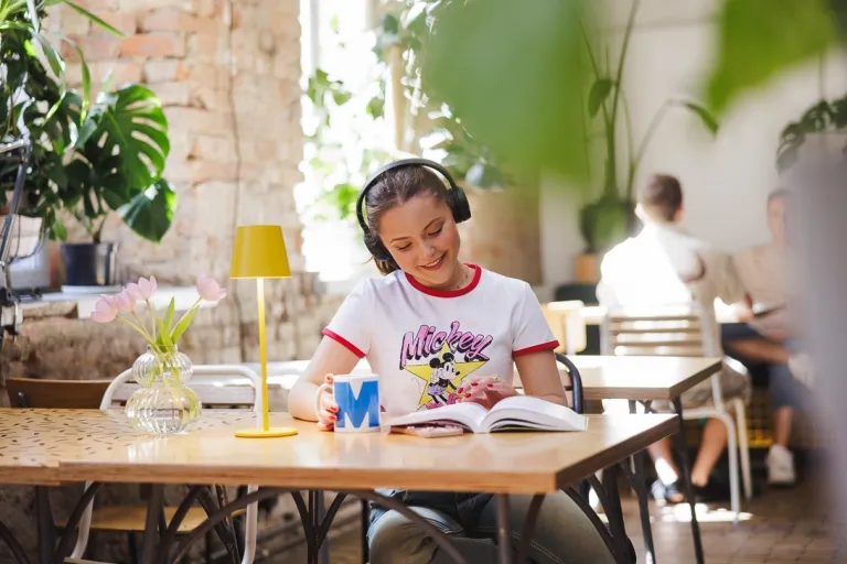 Studentka w słuchawkach siedzi w kawiarni przy książce