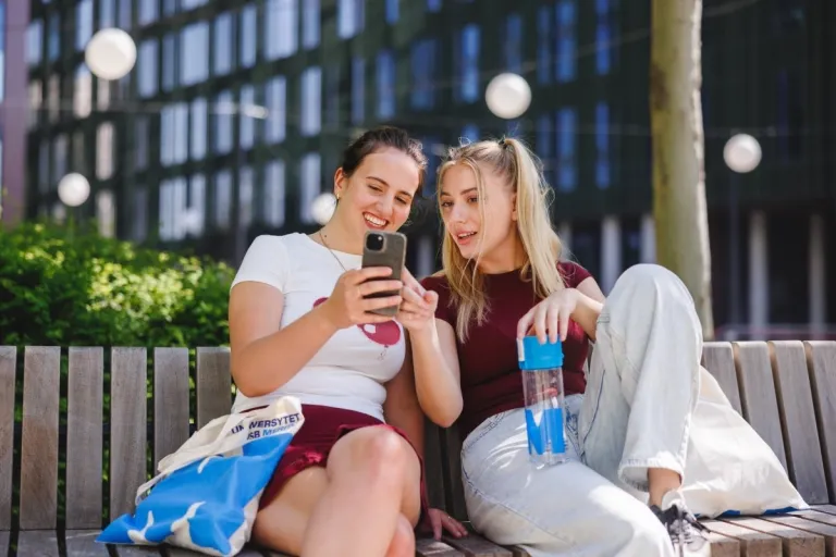 Zapraszamy na Rodzinny Piknik Zdrowia i Uśmiechu | Aktualności | Uniwersytet WSB Merito w Gdańsku: Studentki na ławce przeglądają telefon