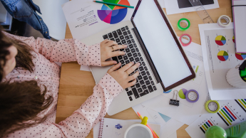 Front-end Developer | Studia I stopnia w Gdyni | Uniwersytet WSB Merito Gdynia: Kobieta pisze na komputerze wśród kartek z wykresami