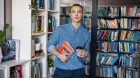 Front-end Developer | Studia I stopnia w Gdyni | Uniwersytet WSB Merito Gdynia: Student z książkami i kawą w ręku w przestrzeni biblioteki