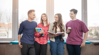 Kadry i płace | Studia I stopnia w Gdyni | Uniwersytet WSB Merito Gdynia: Zdjęcie studentów opierających się o parapet, z tyłu świeci słońce. Na zdjęciu znajduje się dwóch chłopaków i dwie dziewczyny, które zajmują centralne miejsce i trzymają książki