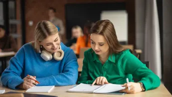Projektowanie interfejsów graficznych | Studia podyplomowe w Gdyni | Uniwersytet WSB Merito Gdynia: dwie dziewczyny siedzą przy biurku i pochylają się nad zeszytami
