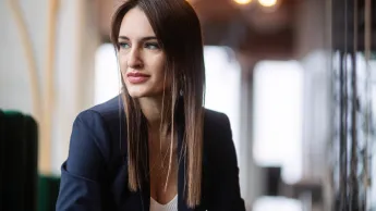 Data Scientist | Studia podyplomowe w Gdyni | Uniwersytet WSB Merito Gdynia: Zdjęcie biznesowe kobiety o długich blond ciemnych włosach znajdującej się w przestrzeni kawiarni. Jest ona ubrana biznesowo i pracuje przy laptopie. Patrzy w bok
