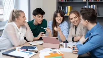 Terapia pedagogiczna z elementami arteterapii | Studia I stopnia w Gdyni | Uniwersytet WSB Merito Gdynia: studenci siedzą przy stole rozmawiając i pracując nad projektem