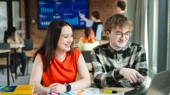 Product Manager w erze AI - zarządzanie produktami cyfrowymi | Studia podyplomowe w Gdyni | Uniwersytet WSB Merito Gdynia: Studentka i student siedzą wspólnie przy biurku. 