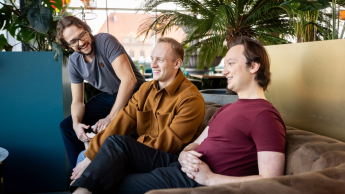 Trzej studenci siedzą wspólnie na kanapie i rozmawiają