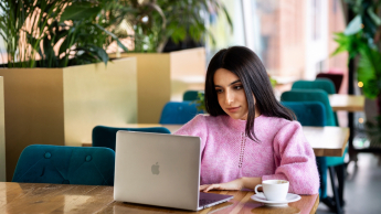 Studentka siedzi w kawiarni z laptopem i kawą.