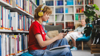 Studentka ze słuchawkami w uszach, książką na kolanach i telefonem w ręku