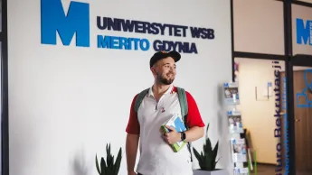 Kadry i płace | Studia I stopnia w Gdyni | Uniwersytet WSB Merito Gdynia: Student na korytarzu przy logo Uczelni