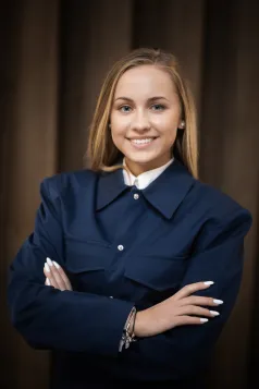 Szkoły | Uniwersytet WSB Merito Gdynia: Zdjęcie młodej dziewczyny o blond włosach i dużym białym uśmiechu. Ma ona na sobie granatową marynarkę