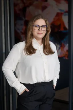 Poznaj nas | Uniwersytet WSB Merito Gdynia: Zdjęcie biznesowe studentki w dużych czarnych oprawkach i blond włosach to ramion. Jest ubrana w klasyczny biznesowy strój - biała koszula i czarne spodnie na kant