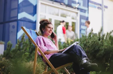 Zapraszamy na sesję, ale spokojnie – tylko zdjęciową! | Aktualności | Uniwersytet WSB Merito Gdynia: Studentka rozmawia przed kampusem przez telefon i leży na leżaku