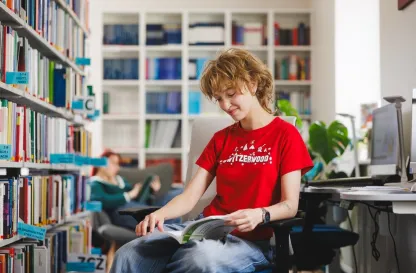 Aktualności | Uniwersytet WSB Merito Gdynia: Studentka w bibliotece przegląda książkę 