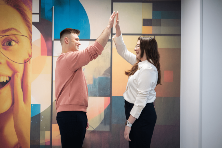 Szkoły | Uniwersytet WSB Merito Gdynia: studenci przybijający sobie piątkę na tle kolorowej fototapety