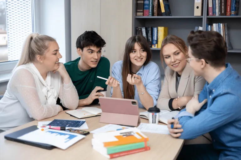 Zobacz nasze szkoły partnerskie | Uniwersytet WSB Merito Gdynia: studenci siedzą przy stole rozmawiając i pracując nad projektem